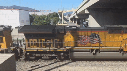 Yellow locomotive 7049 leads a train under a Burbank overpass.