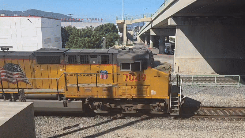 Yellow locomotive 7049 leads a train under a Burbank overpass.