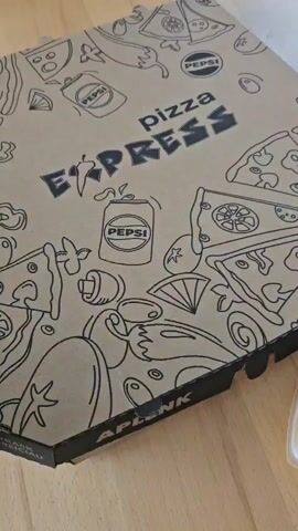 The video begins with a close-up of a Pizza Express pizza box adorned with a playful black and white line drawing of pizzas and Pepsi cans. The box is closed. The scene then transitions to an aerial shot revealing the contents of the open pizza box: a whole pizza with a variety of toppings. The camera then zooms in on the pizza, showcasing its crust, cheese, pepperoni slices, green pepper rings, sliced mushrooms, black olives, and a drizzle of dark sauce, possibly barbecue sauce. The lighting is natural, suggesting the video was filmed indoors during the day, likely on a wooden surface.