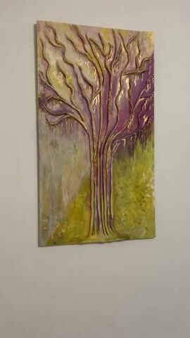 The video shows a close-up, panning shot of a textured artwork depicting a tree with elaborate branches. The artwork appears to be a mixed-media piece, featuring raised elements, possibly sculpted with clay or a similar material, and painted in shades of purple, yellow, and gold. The branches are outlined in gold, and some areas have a dripping effect, adding to the texture and visual interest. The background is a blend of light grey and yellow, with hints of green on the right side, suggesting foliage or a landscape. The artwork is hanging on a plain, light-colored wall, indicating it is likely displayed indoors. The lighting is soft, with no harsh shadows, suggesting it might be daytime or a well-lit indoor space. There is no visible text or identifiable people in the media. The overall mood of the artwork and its presentation is one of artistic expression, focusing on the organic form of a tree with a touch of opulence due to the gold accents.