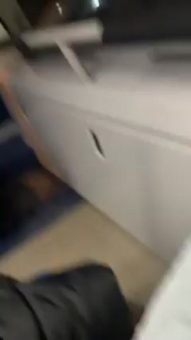 The video shows a person sitting on a bus at night. The bus is moving along a road lined with trees. A car's headlights are visible ahead. The interior of the bus has blue seats and white panels. The lighting is dim.