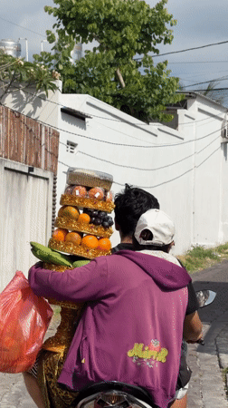 Ornate fruit offering stand being transported by scooter in Bali