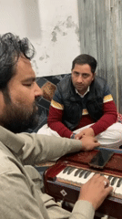 Man performs harmonium music with child drummer in indoor session