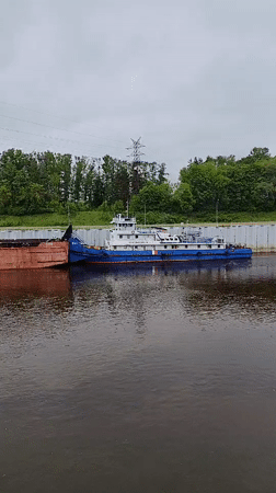 Tugboat pushes barge through Rybinsk river lock early morning