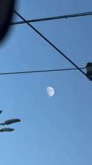 Crescent moon over a sun-lit city on a clear afternoon