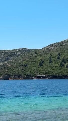 A boat is sailing on a blue sea near a green, tree-covered island. The sky is clear and blue.