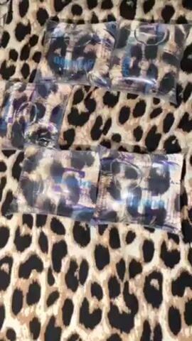 The video shows a collection of small, sealed packages arranged on a surface with a leopard print pattern. The packages appear to contain items with dark and light elements visible through the transparent packaging. The leopard print background is made up of tan-colored circles with dark brown or black spots. The packages are arranged in rows and columns, taking up much of the frame. The camera pans slightly to the right, revealing more packages, before stopping. No people are visible in the video.