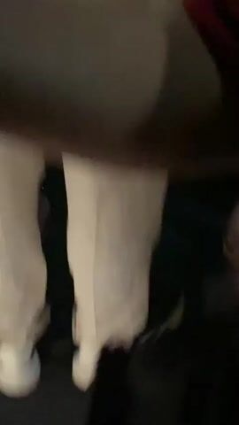 The video opens with a close-up shot of someone's feet wearing red, white, and blue striped socks and black sneakers. The camera then pans to a dark scene with a glimpse of a person in a light-colored shirt and then to a lively nightclub scene. A DJ, wearing a white t-shirt, is seen behind a DJ booth, manipulating controls on a DJ setup. A crowd of people is gathered around, with many raising their hands in the air, dancing, and enjoying the music. The atmosphere appears energetic and celebratory.