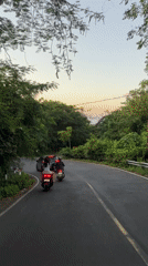 Scooter riders follow dark car on winding Kuta road