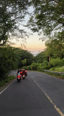 Scooter riders follow dark car on winding Kuta road