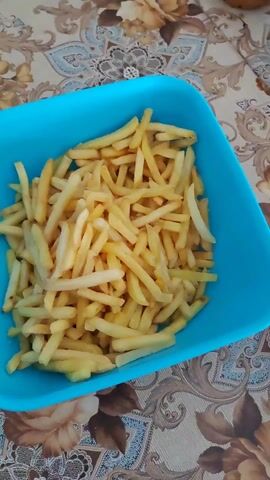 The video shows a blue plastic container filled with french fries on a table with a floral tablecloth. The camera moves closer to the fries.