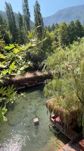 Riverside restaurant with thatched huts over clear water, Alanya
