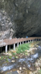 Tourists walk wooden walkway near cave entrance in Zhangjiajie
