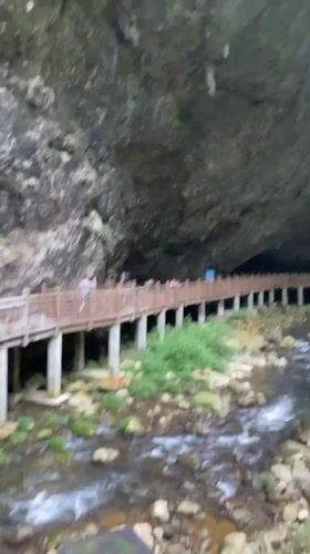 Tourists walk wooden walkway near cave entrance in Zhangjiajie
