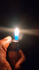 Person holds lit lighter with blue-white flame in darkness