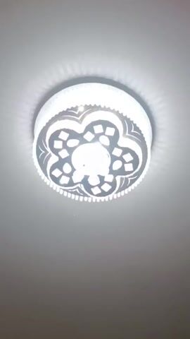 The video shows a ceiling light fixture. The light is round with a flower-shaped design. The brightness of the light changes between warm white, bright white, and blue-tinted white as the video plays. The ceiling is a light neutral color.