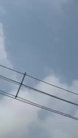 The video is a vertical shot of a cloudy, gray-blue sky. The clouds are white and fluffy, with varying shades of gray. At 0:02, the corner of a street sign briefly enters the frame from the right side. There is a loud noise at the beginning of the video.
