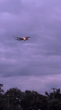 Plane with landing lights crosses purple cloudy sky over Chiang Mai