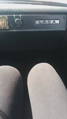 The camera shows the interior of a car, specifically the passenger seat and the interior panel. The word "LADA" is embossed on the panel. The passenger seat appears to be covered with a gray fabric. There is nothing else discernible in the video.