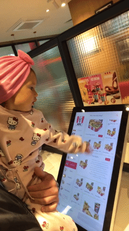 Child in pink Hello Kitty outfit uses KFC kiosk