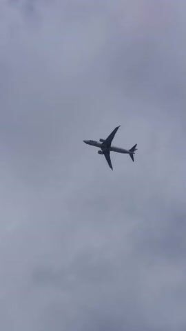 The video shows a commercial airplane flying in a cloudy sky. The plane is a passenger jet with two engines mounted under its wings. It is flying at an angle, appearing to be in the process of banking or turning. The sky is overcast with a mix of white and gray clouds, suggesting it is daytime, possibly late morning or afternoon. There are no people or distinct landmarks visible in the frame, offering little specific location context beyond what's provided. The overall mood is neutral, focusing on the aerial movement of the aircraft against the backdrop of the cloudy sky.