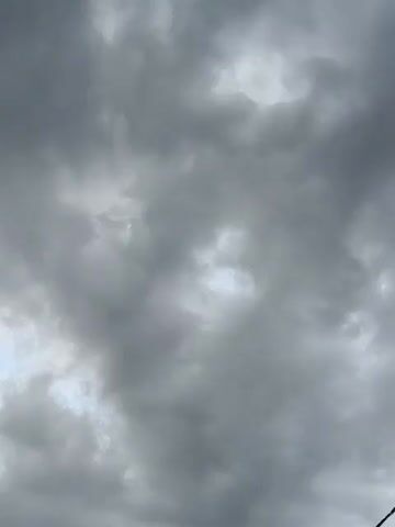 The video shows a cloudy sky. The clouds are gray and appear to be moving. There is some light filtering through the clouds in places, suggesting it may be daytime. The camera is looking straight up at the sky. There are no people, objects, or actions visible in the video. The environment is purely the sky and clouds.