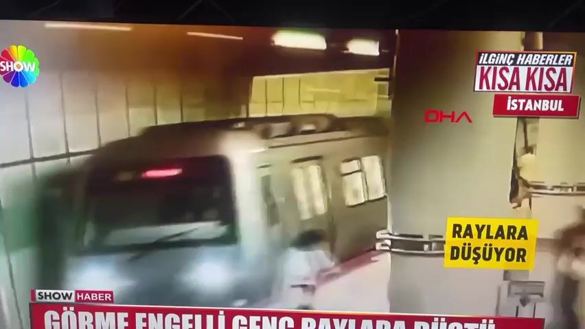 The video shows a news report with several scenes. The first scene shows a train at a subway station, with a person falling onto the tracks. The second scene shows emergency responders helping a person who appears to have fallen on an escalator. The third scene shows people gathered around the person on the escalator. There is text overlays indicating this is "SHOW HABER" reporting on an "INTERESTING NEWS" story in "ISTANBUL" about a "BLIND YOUNG PERSON FALLING ONTO THE TRACKS."