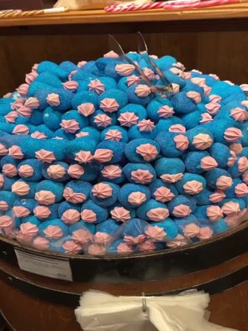 The video shows a display of various candies in a store. There are marshmallows, gummy worms, and fruit-shaped gummies. The candies are presented on wooden barrels and in wooden chests. The candies are colorful and attractively arranged.