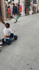 Man guides child on toy ATV in Calella pedestrian area