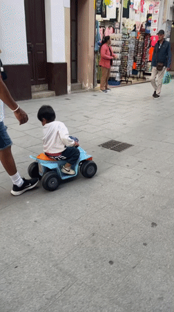 Man guides child on toy ATV in Calella pedestrian area