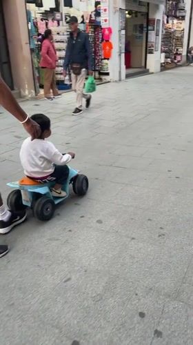 Man guides child on toy ATV in Calella pedestrian area