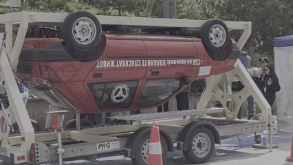 Overturned red car displayed on trailer at organized event