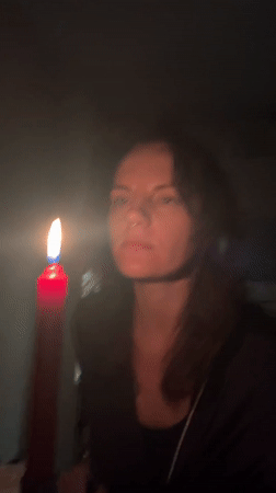 Woman extinguishes red candle in darkened Montenegro room