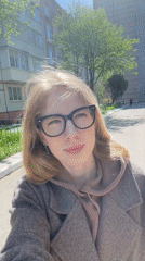 Woman in brown coat observed walking, taking selfie in Izhevsk