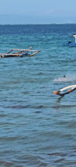 Morning beach activity observed in Denpasar with swimmers and boats