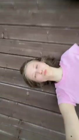 The video begins with a close-up of a person's face looking towards the camera, with a wooden wall in the background. The video then transitions to a view of a person sitting on a wooden deck, looking out at a sunset. The sunset is vibrant with orange and pink hues. The camera pans across the sky, showing clouds and the silhouette of trees and houses against the colorful sky.