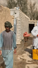 Hazmat-suited workers prepare spraying equipment in rural Kandahar