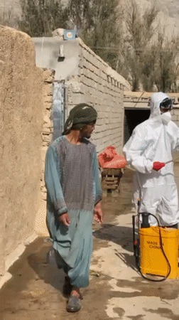 Hazmat-suited workers prepare spraying equipment in rural Kandahar