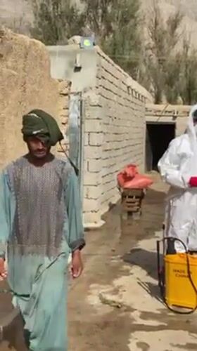 Hazmat-suited workers prepare spraying equipment in rural Kandahar
