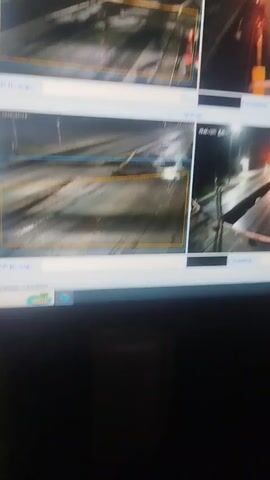 The media file displays a multi-camera security system showing a road in Kyrgyzstan at night. The road appears wet, suggesting it is raining or has recently rained. Streetlights illuminate the scene, reflecting off the wet asphalt. In one of the camera feeds, a car is visible driving on the road. The system displays timestamps and camera labels in Russian, such as "Түндүк айланып өтүүчү жол 84 га" (North Bypass Road 84 km). Other visible text includes "госномер" (license plate) and dates like "29-01-2023". The overall scene depicts a typical night on a highway in a somewhat rural or developing area.
