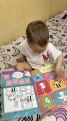 Toddler reads colorful book on bed in Rusanovo