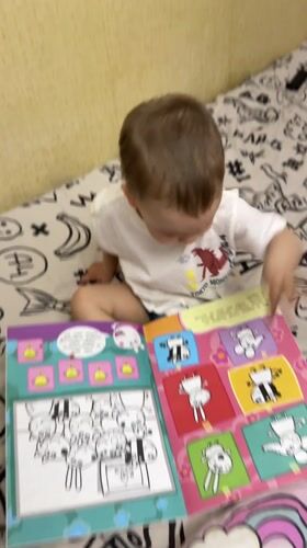 Toddler reads colorful book on bed in Rusanovo