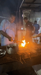 Street vendors cook meat skewers at night stalls in Ado
