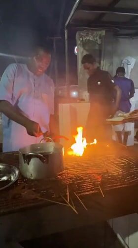 Street vendors cook meat skewers at night stalls in Ado