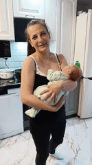 Mother holds baby in kitchen, smiles for camera