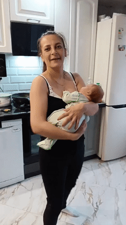 Mother holds baby in kitchen, smiles for camera