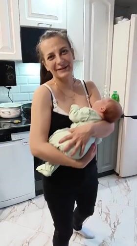 Mother holds baby in kitchen, smiles for camera