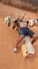 Man weightlifts on makeshift bench in outdoor Bukuru setting