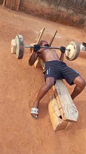 Man weightlifts on makeshift bench in outdoor Bukuru setting