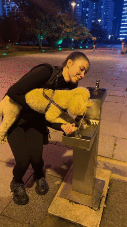 Woman helps dog drink from public fountain in Batumi